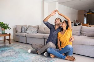 Young couple sitting on the floor of their UAE living room forming a roof shape with their hands, symbolising home insurance protection