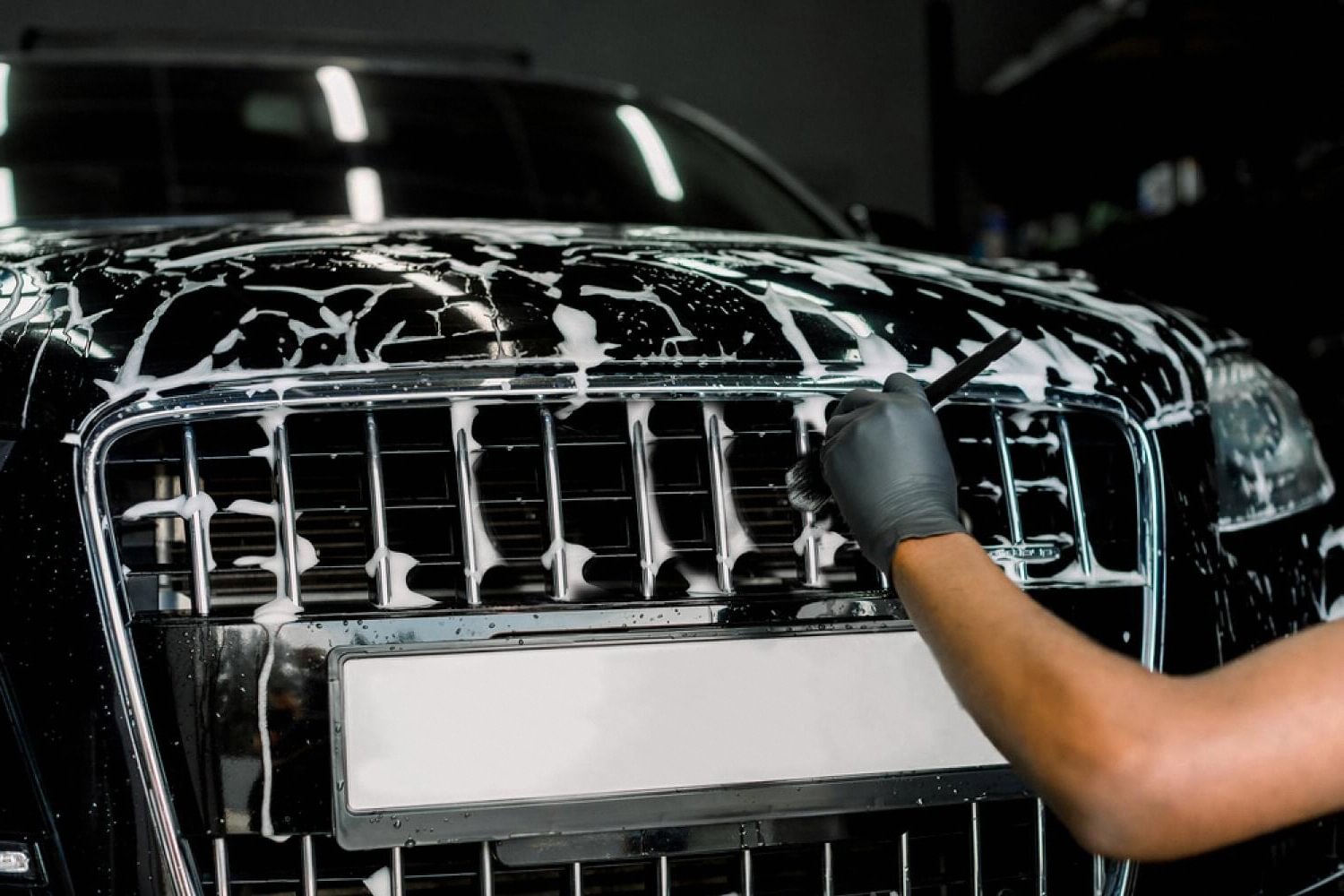 Detailer brushing soap on a car grille during pre-coating prep